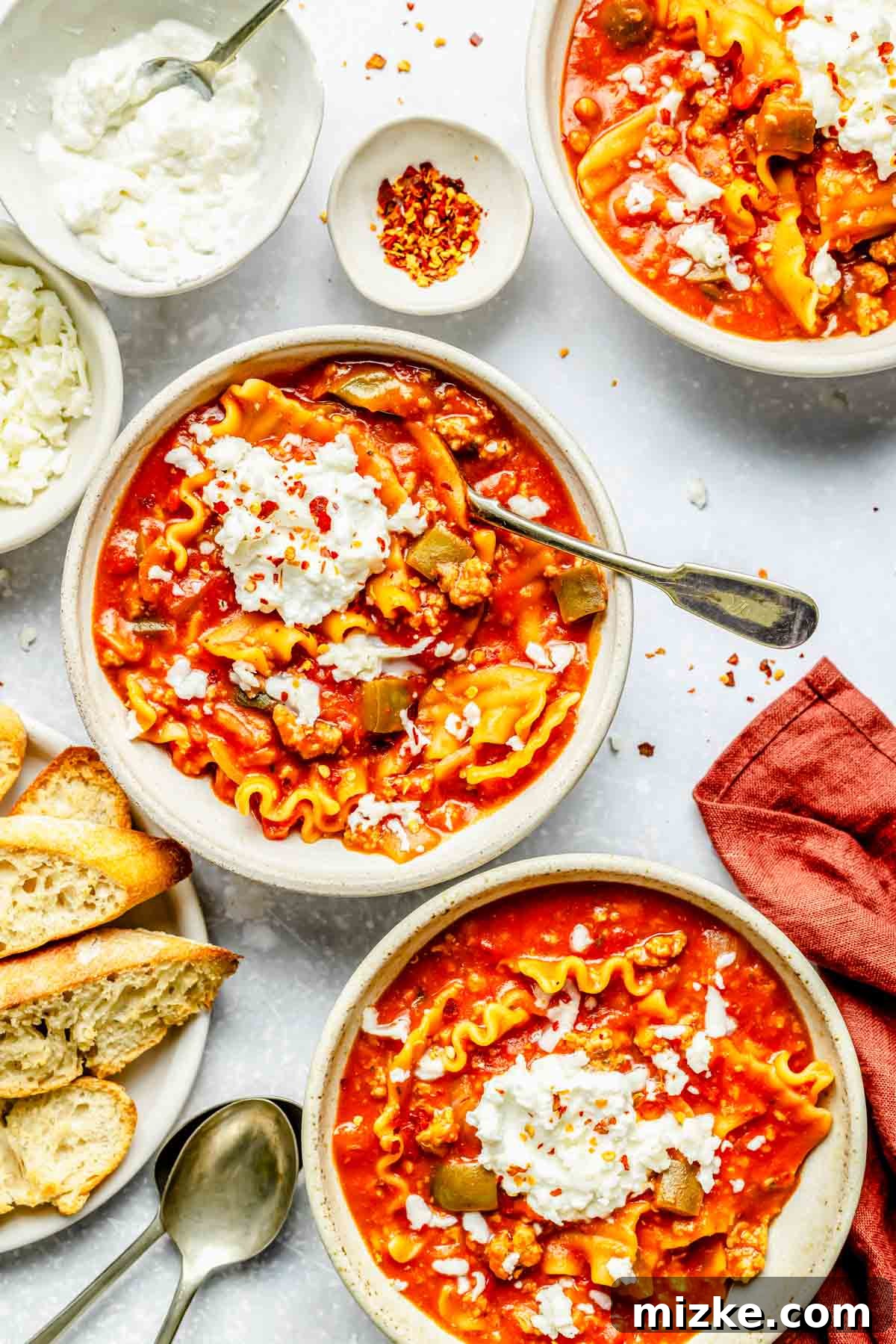 One-Pot Lasagna Soup 2 three bowls of lasagna soup with ricotta topping next to toasted bread