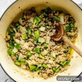 green bell peppers, onions, and crumbled sausage in a large dutch oven with a wooden spoon