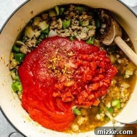 chicken stock being poured into the pot with tomato sauce, diced tomatoes, salt, and red pepper flakes added to sausage, onions, and bell peppers