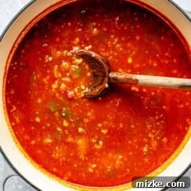tomato liquid added to a large dutch oven with a wooden spoon