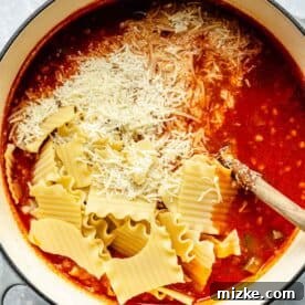 broken lasagna noodles and parmesan cheese added to the pot of soup