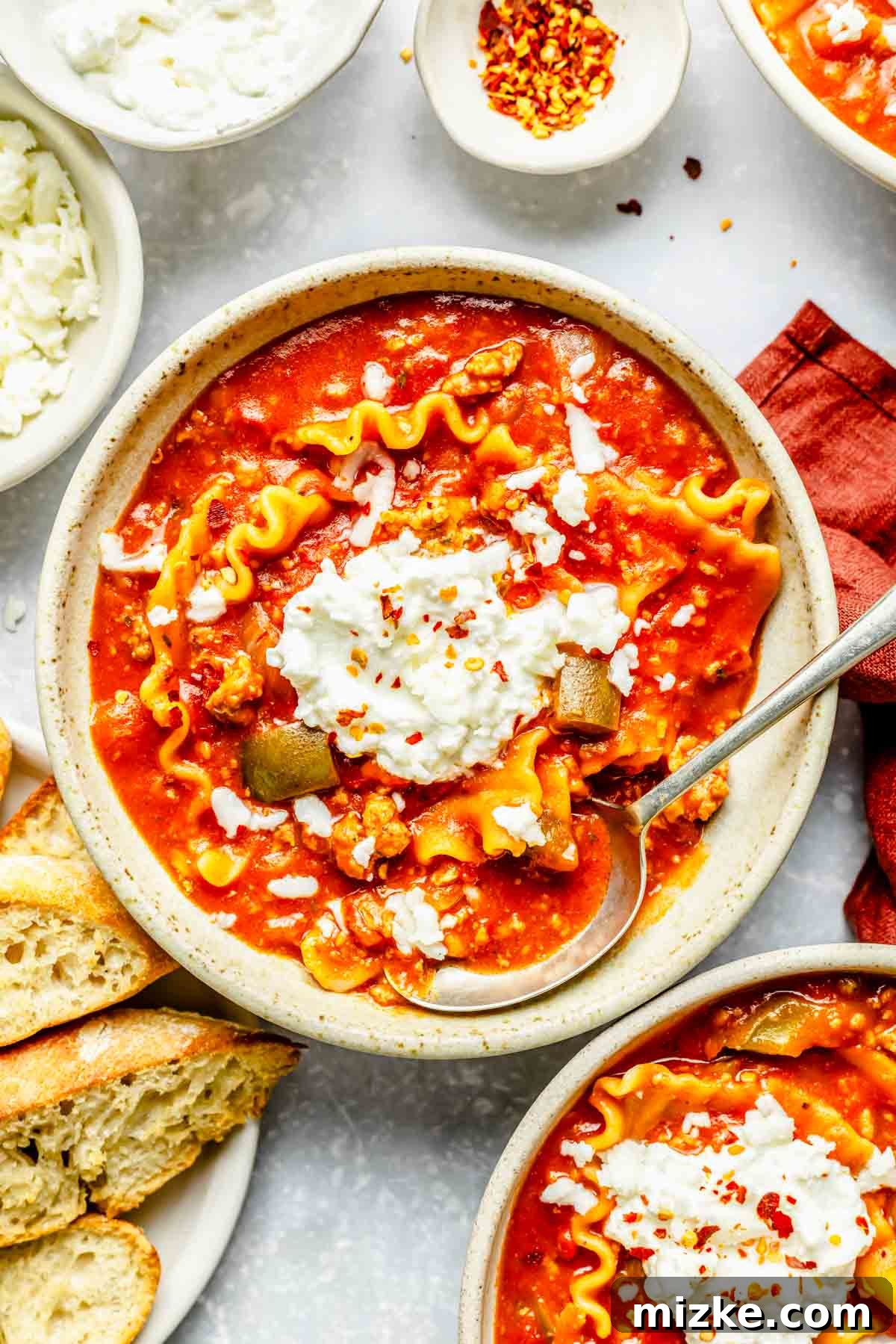 One-Pot Lasagna Soup 4 a bowl of lasagna soup with a dollop of ricotta cheese on top and a metal spoon next to toasted bread