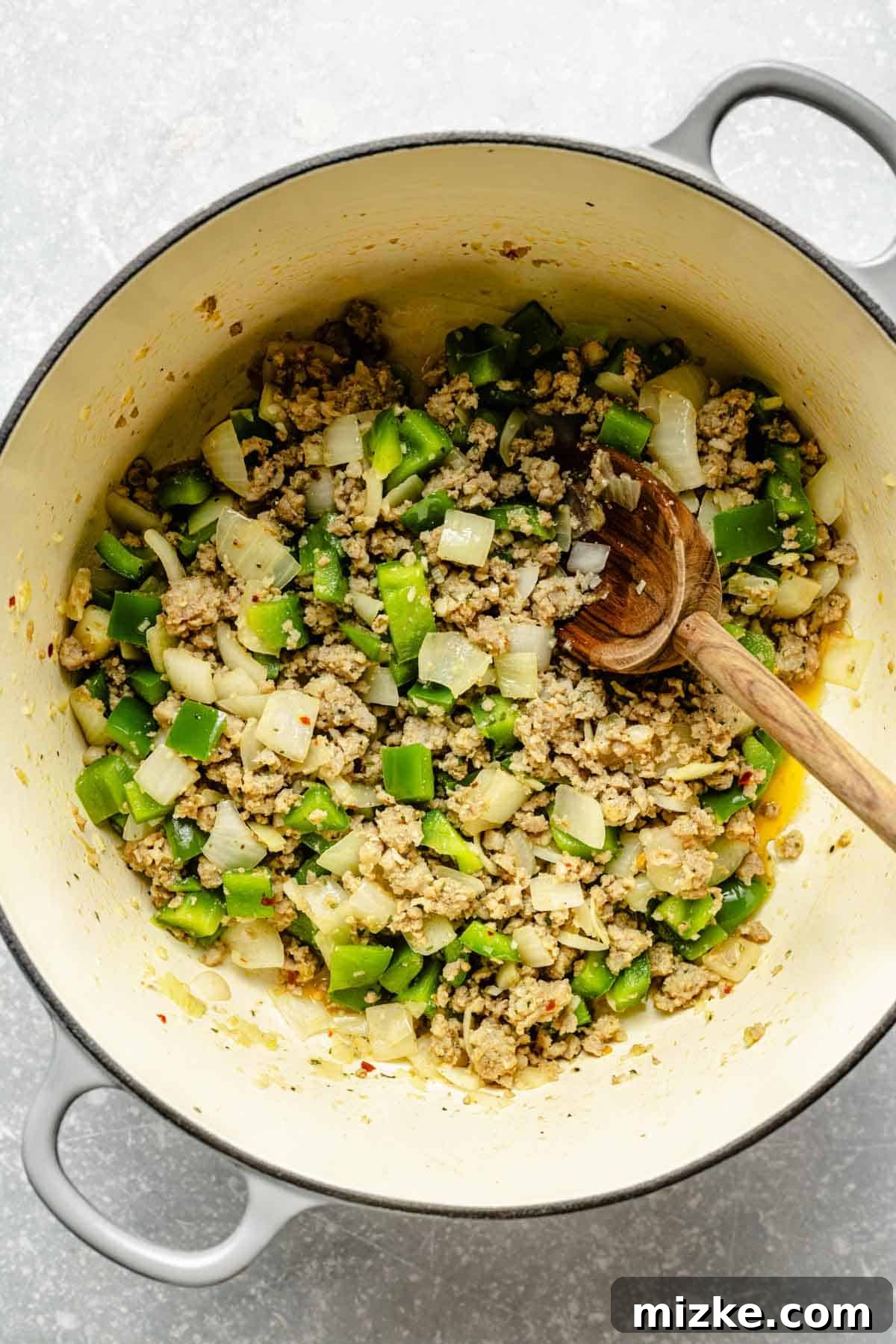 One-Pot Lasagna Soup 5 green bell peppers, onions, and crumbled sausage in a large dutch oven with a wooden spoon