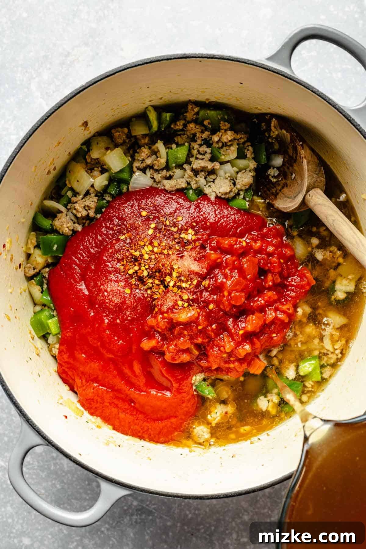 One-Pot Lasagna Soup 6 chicken stock being poured into the pot with tomato sauce, diced tomatoes, salt, and red pepper flakes added to sausage, onions, and bell peppers