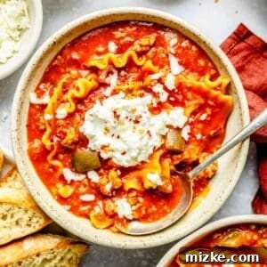 a bowl of lasagna soup with a dollop of ricotta cheese on top and a metal spoon next to toasted bread