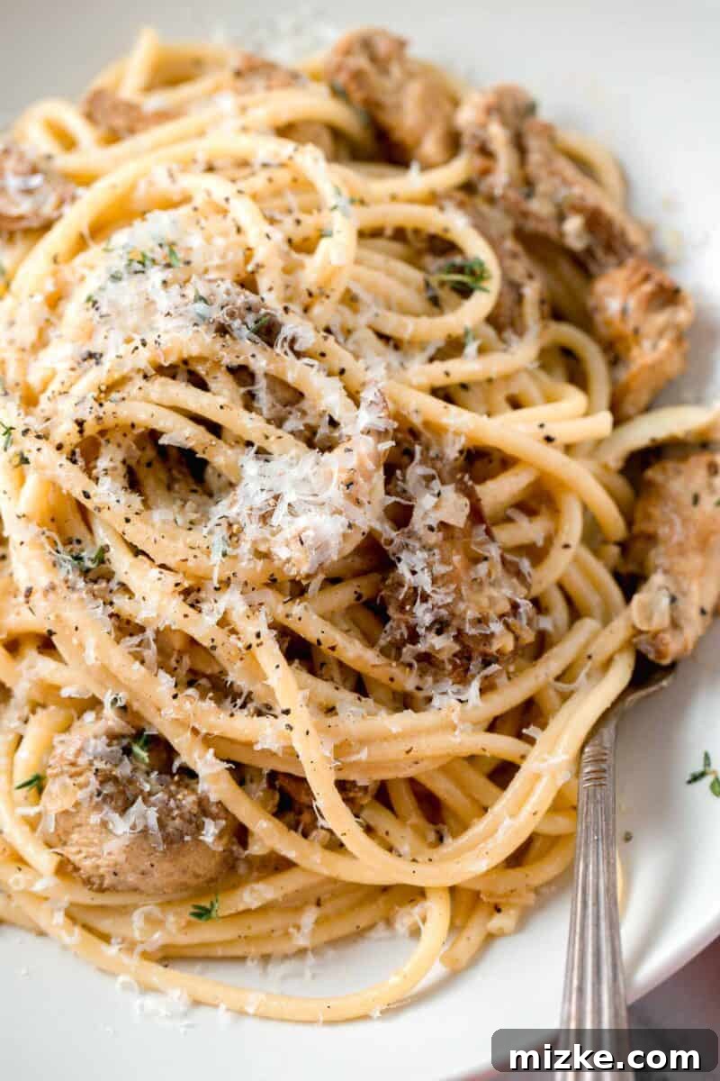 Velvety Lion's Mane Mushroom Pasta 3 creamy lions mane pasta in a white bowl with a metal fork and fresh parmesan and cracked black pepper sprinkled on top