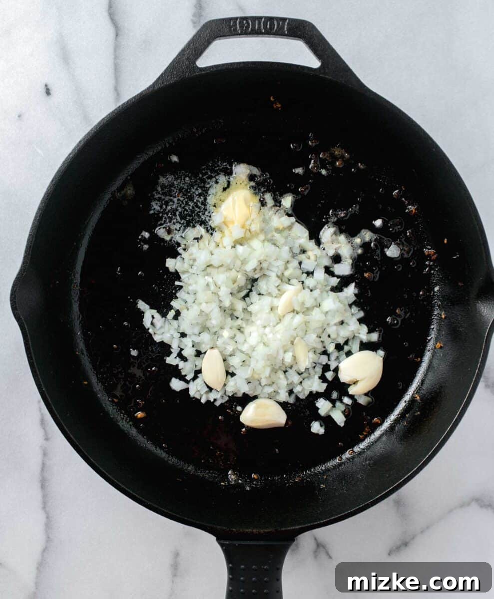 Velvety Lion's Mane Mushroom Pasta 4 whole, smashed garlic cloves with onion being sautéed in a cast iron skillet with butter