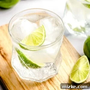 A perfectly prepared gin and tonic on a cutting board with a slice of lime in the background.