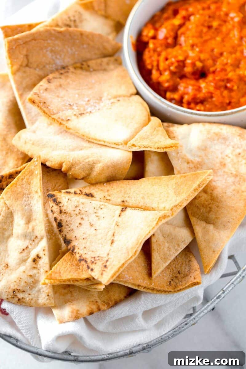 Crispy Air Fryer Pita Chips 6 A bounty of golden, air-fried pita chips presented in a rustic metal basket, with a tempting red pepper dip waiting alongside.