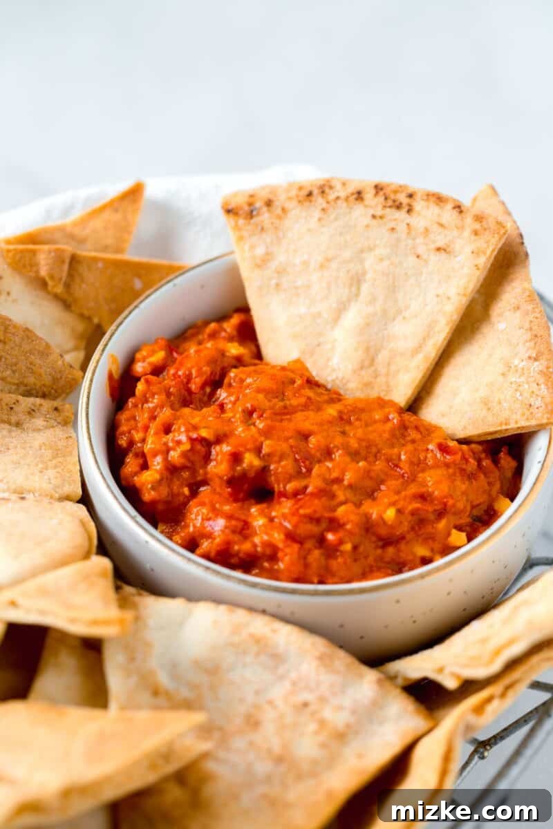 Crispy Air Fryer Pita Chips 8 Two golden, air-fried pita chips gracefully emerging from a rich red pepper dip, nestled amongst a basket full of other crispy chips.