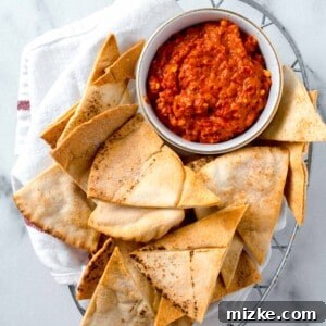 Crispy air-fried pita bread in a metal basket, lined with a linen towel, next to a white bowl of red pepper dip.