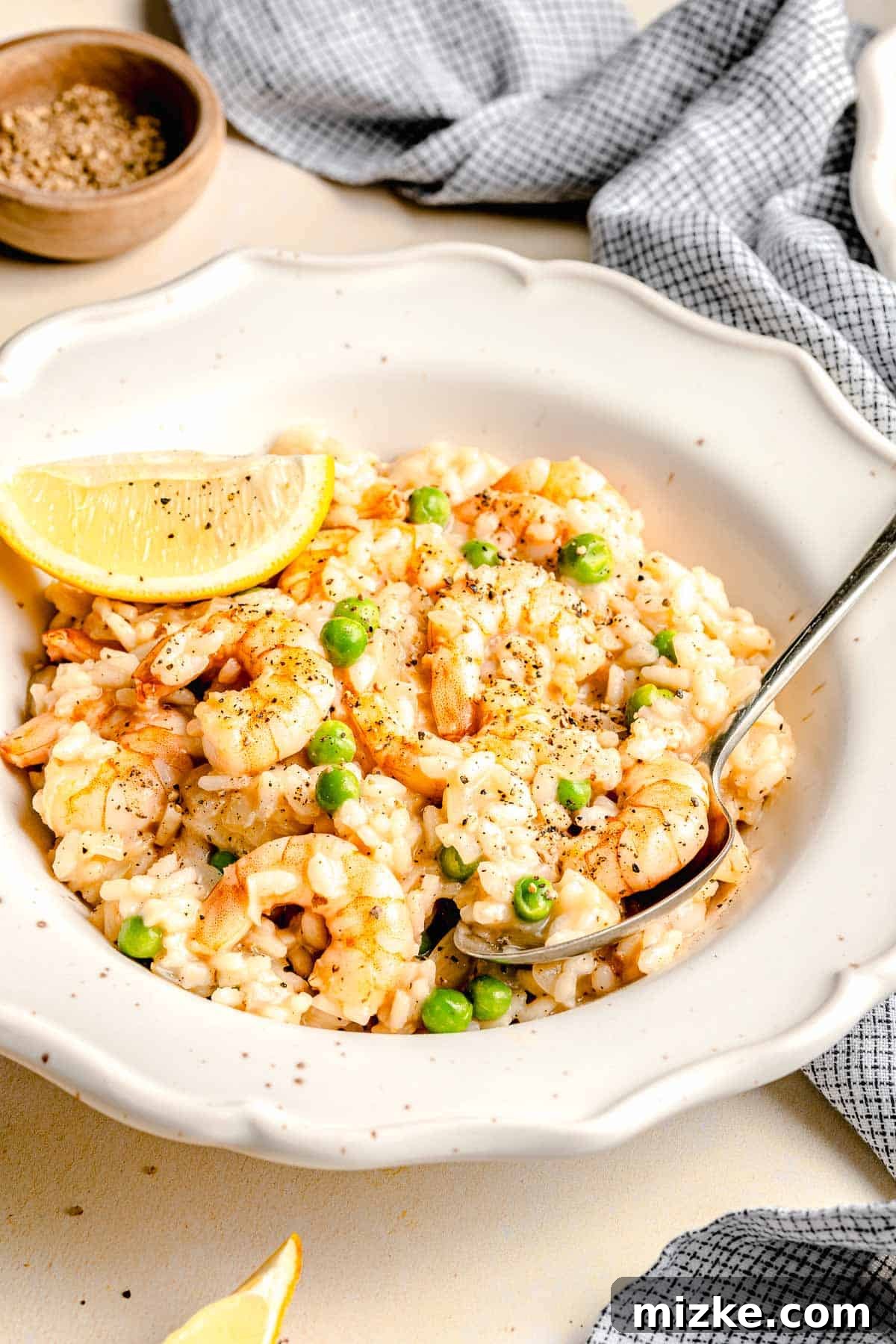 Easy Shrimp Risotto: Succulent shrimp and peas in creamy Arborio rice, flavored with white wine and lemon. Creamy shrimp risotto in a rustic bowl with a serving spoon, garnished with fresh herbs.
