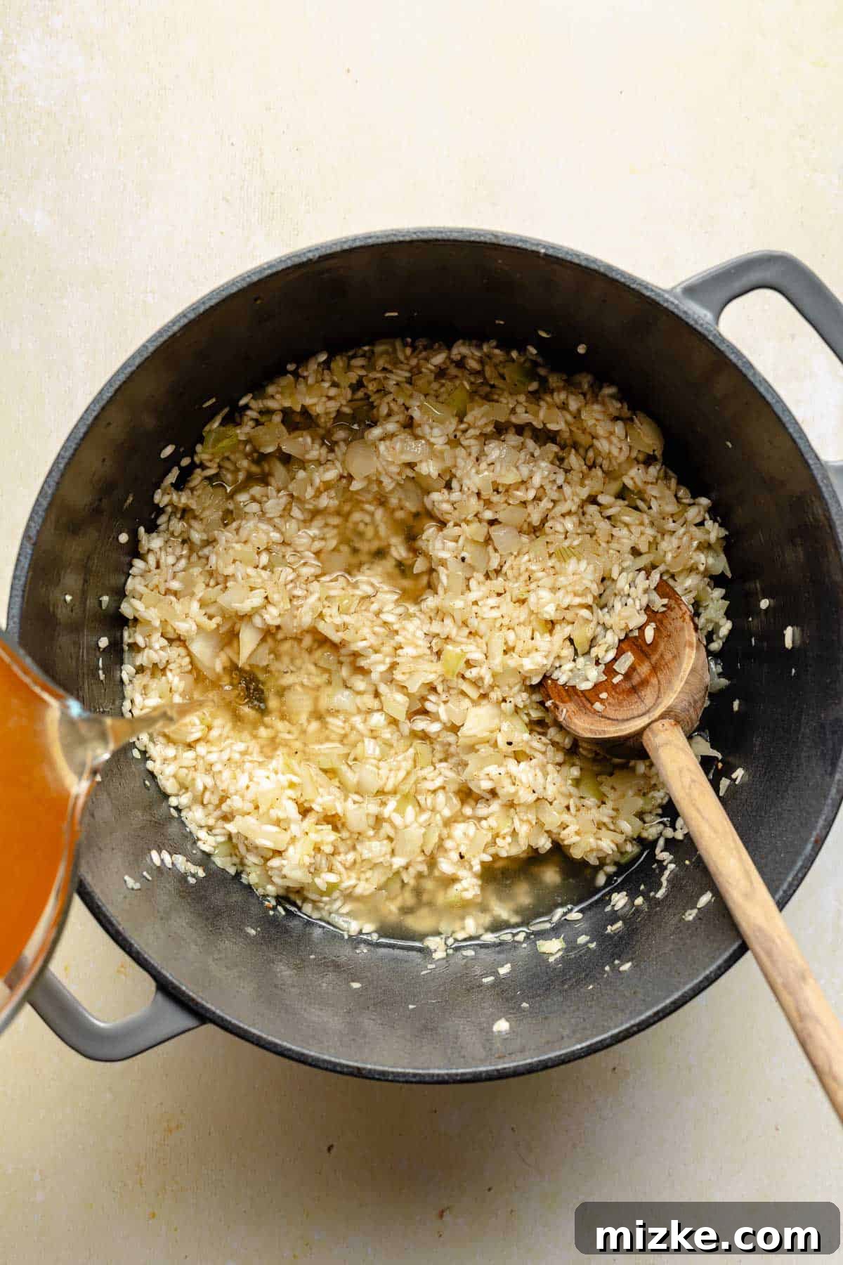 Gradually adding broth to rice for creamy shrimp risotto. Adding warm vegetable broth to Arborio rice in a pot for risotto.