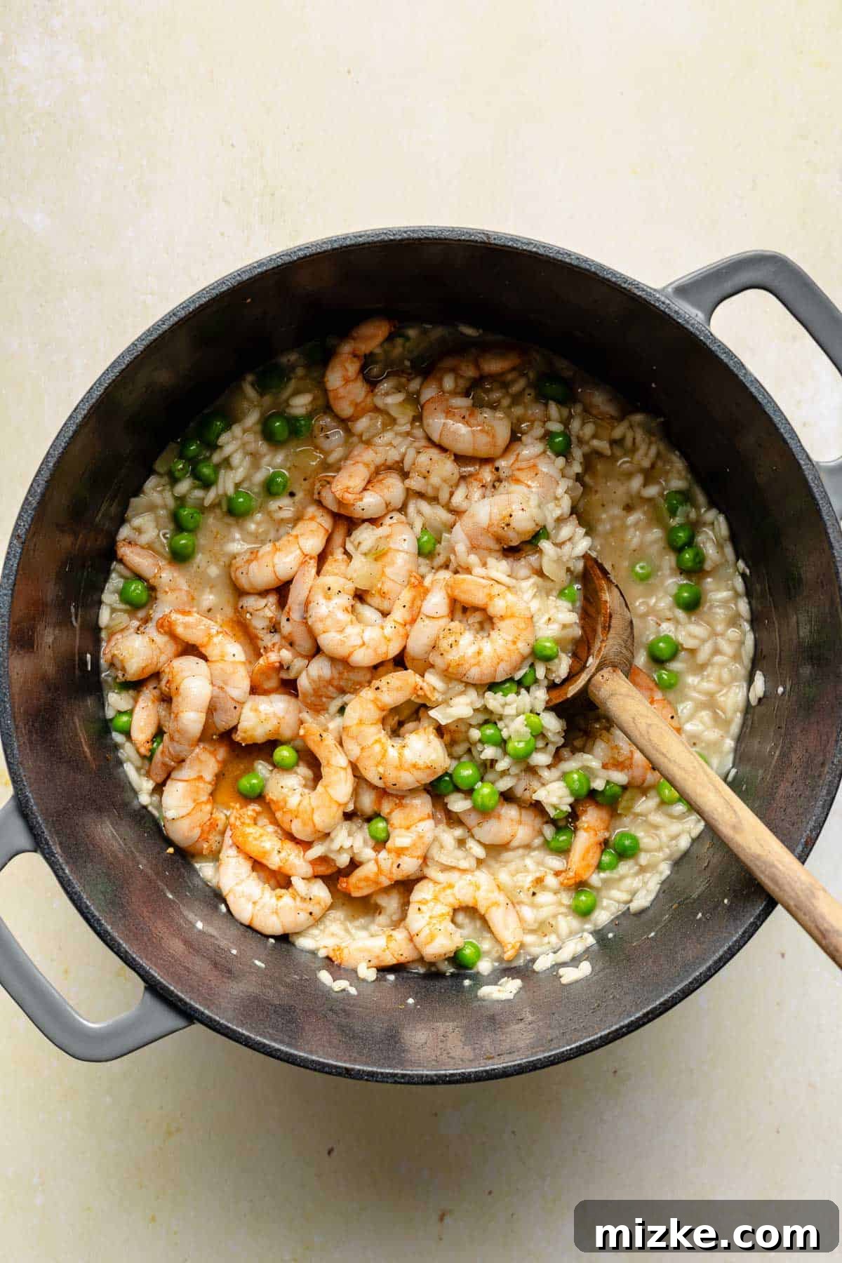 Folding in shrimp and peas to finish a delicious risotto. Stirring cooked shrimp and thawed peas into creamy risotto.