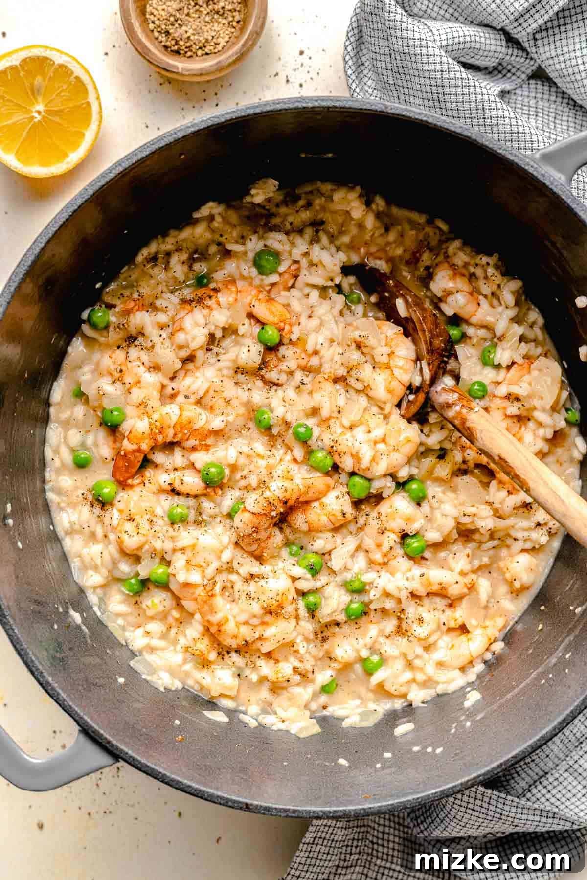 Creamy shrimp and pea risotto in a pot, ready to enjoy. Finished shrimp risotto in a cooking pot with a wooden spoon ready to be served.