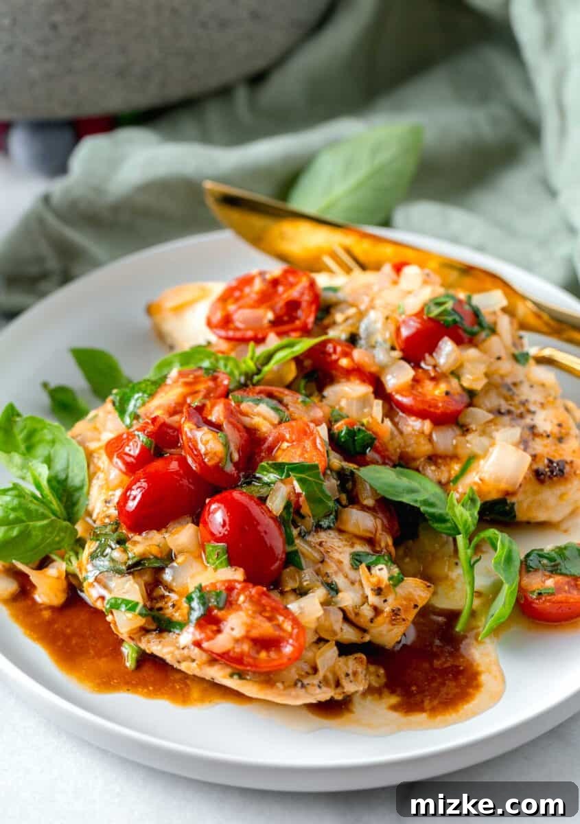 Skillet Roasted Garlic Tomato Basil Chicken 2 chicken breasts plated on a white plate with fresh tomatoes, basil, onions on top with balsamic vinegar drizzled.