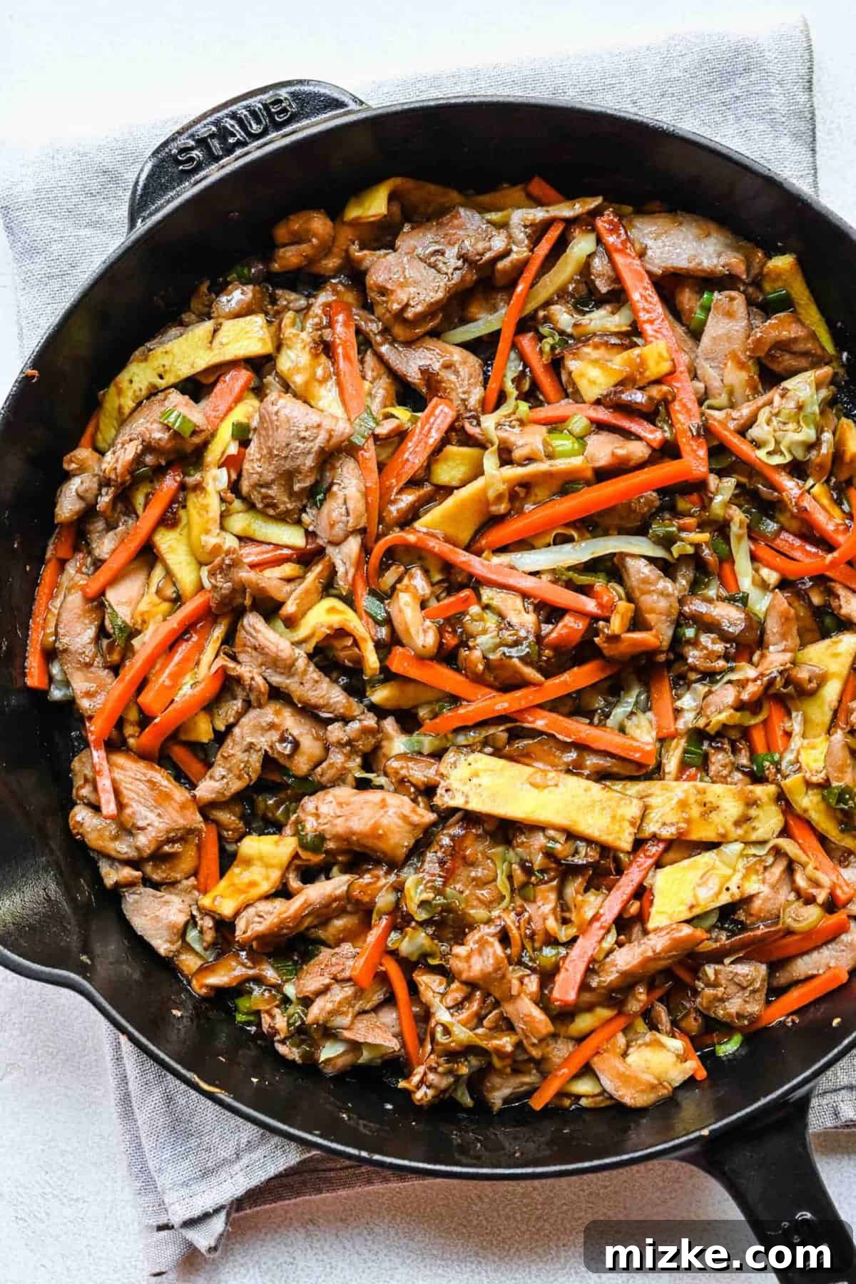Step 7: The final stage of assembly, incorporating the cooked chicken, sauce, and egg into the vibrant vegetable stir-fry. Adding sliced, cooked eggs to a skillet of Moo Shu chicken and vegetables.