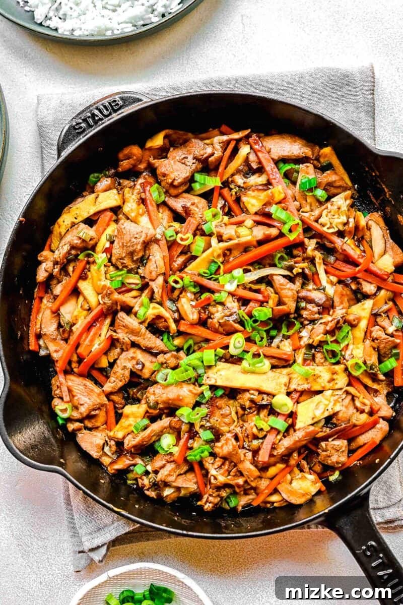 Moo Shu chicken simmering in a skillet, coated in a rich, thickened sauce, ready to be served. Moo Shu chicken stir-frying in a large skillet, glistening with sauce and vibrant vegetables.
