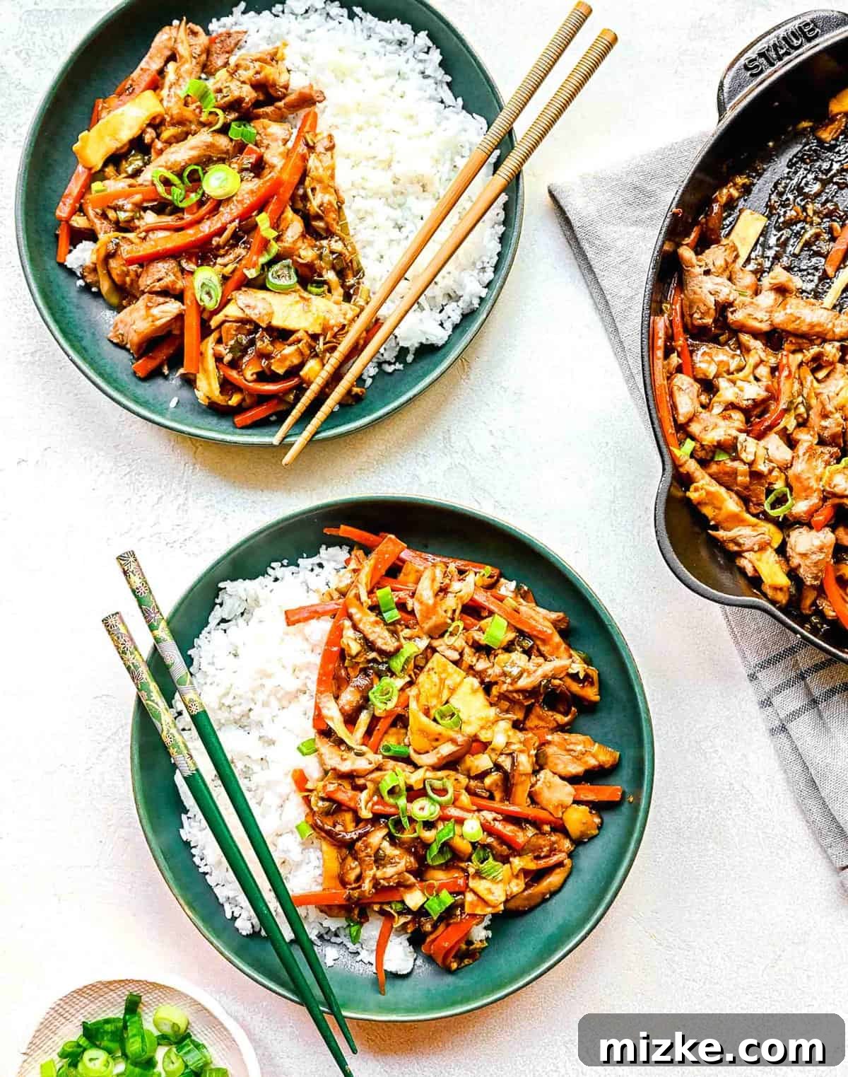 Plated Moo Shu chicken, a perfect blend of chicken, vegetables, and egg coated in a delightful, aromatic sauce. Two plates of Moo Shu chicken served with white rice and chopsticks, ready for a meal.