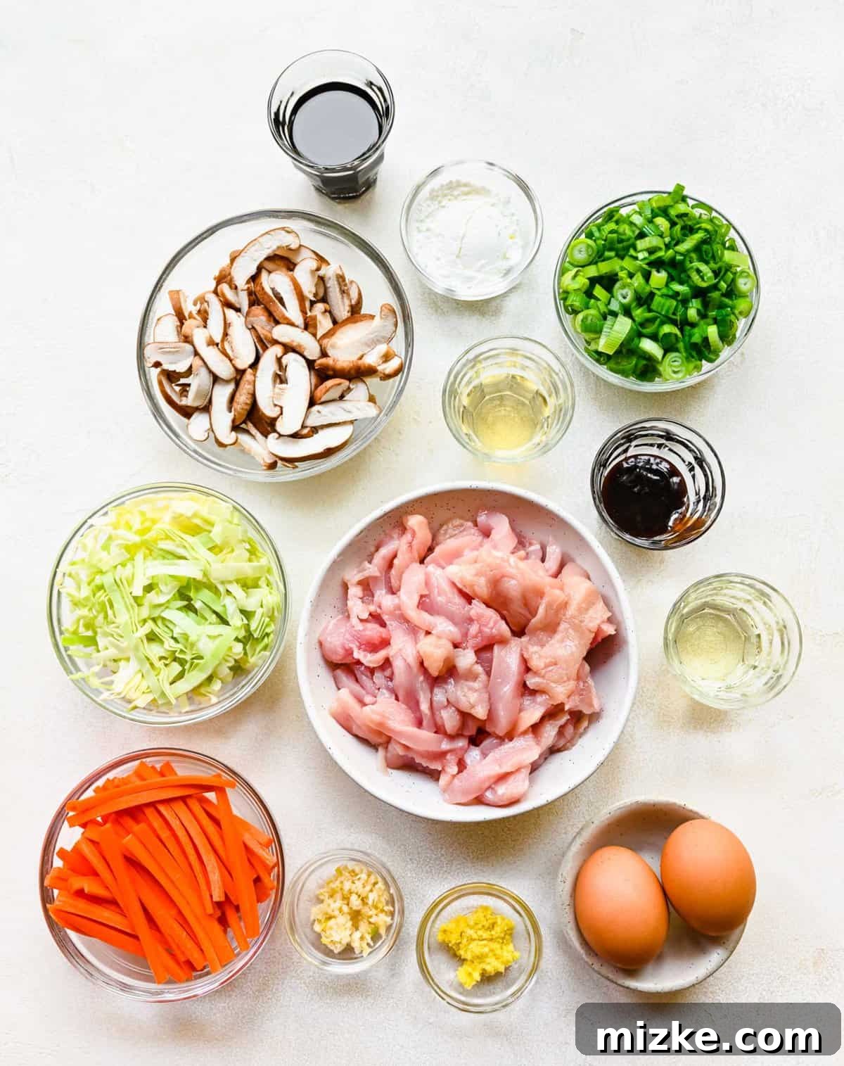 Organized Moo Shu chicken ingredients including sliced chicken, eggs, various vegetables, and sauce components. Ingredients for Moo Shu chicken separated into bowls, ready for preparation.