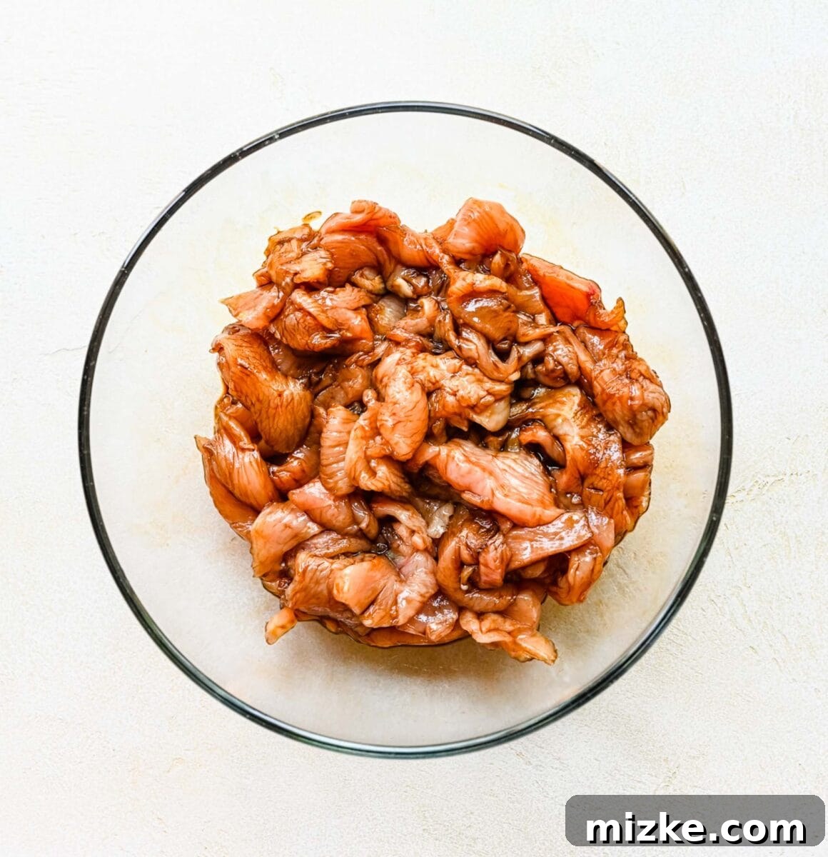 Step 1: Marinating thinly sliced chicken breasts in soy sauce for maximum flavor and tenderness. Thinly sliced chicken marinating in soy sauce in a glass bowl.