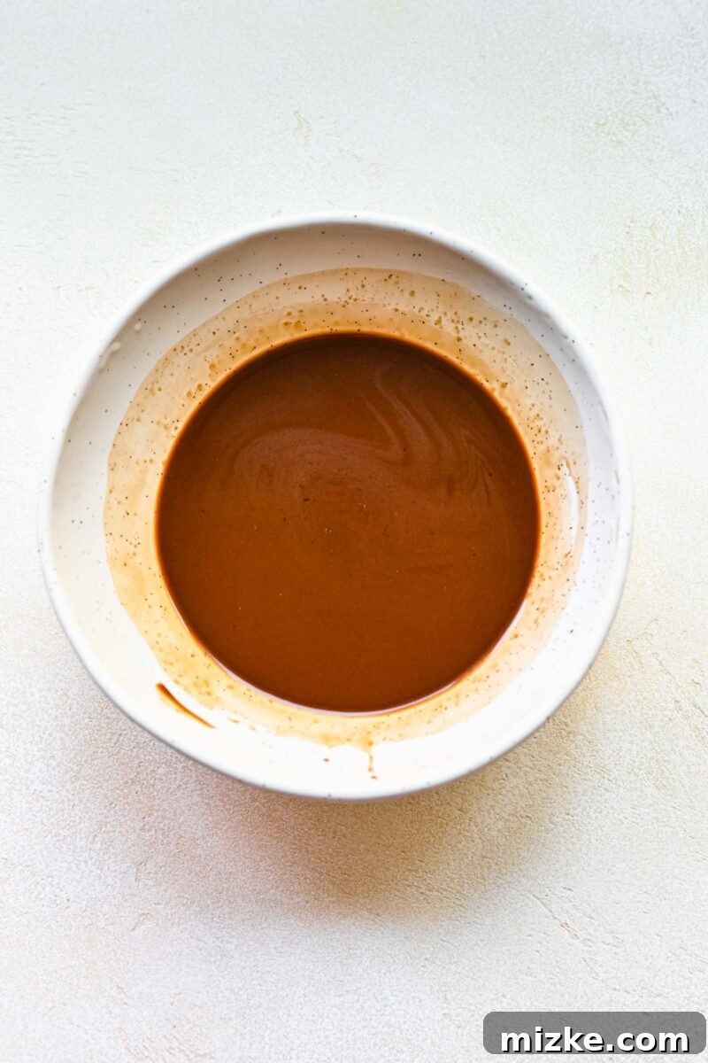 Step 2: Preparing the savory-sweet Moo Shu sauce by whisking hoisin, rice vinegar, cornstarch, and soy sauce. Moo Shu sauce ingredients whisked together in a small ceramic bowl.