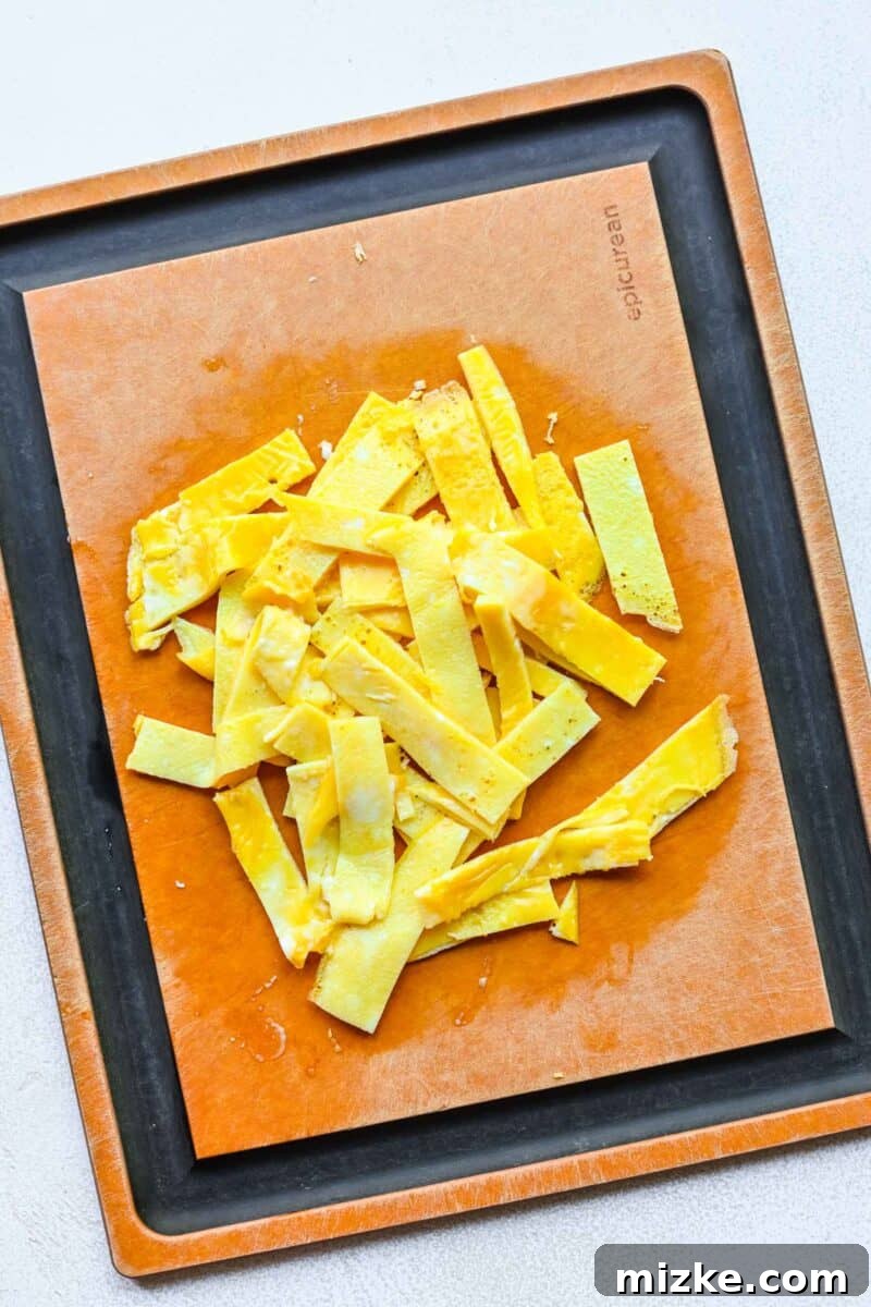 Step 3: Cooking and slicing eggs into thin strips for inclusion in the Moo Shu chicken dish. Cooked, thinly sliced eggs arranged on a cutting board.