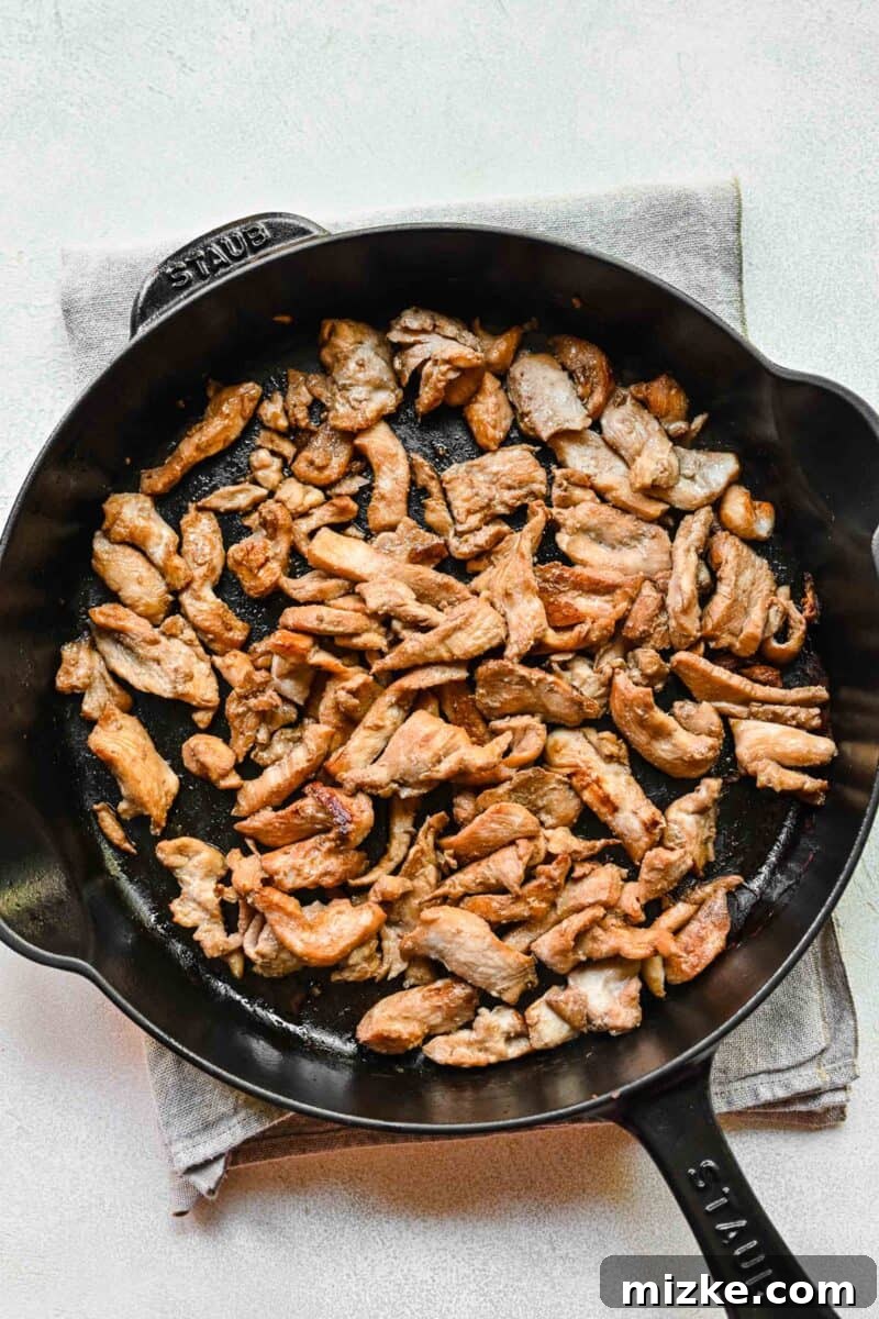 Step 4: Sautéing the marinated chicken slices until beautifully browned and cooked through. Thin slices of chicken browning in a hot pan or wok.