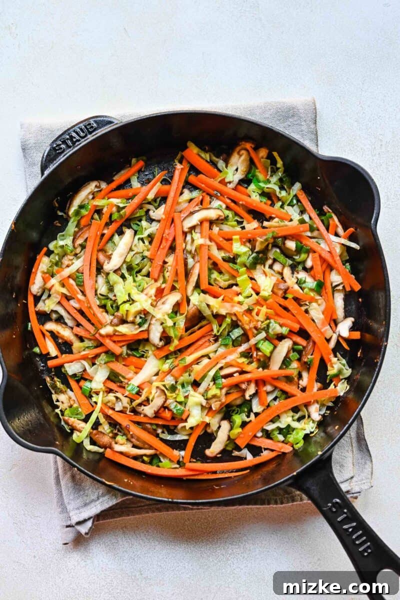 Step 6: Stir-frying the colorful mix of cabbage, carrots, and mushrooms until tender-crisp. Sautéing thinly sliced cabbage, julienned carrots, and mushrooms in a pan.