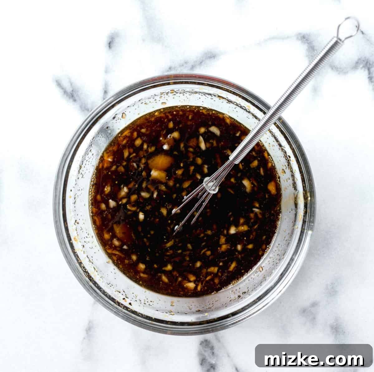 Sauce for honey garlic lemon pepper chicken thighs in a clear bowl whisked together with a metal whisk