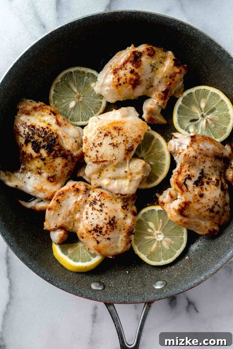 Seared chicken thighs with fresh lemon slices in a grey nonstick skillet