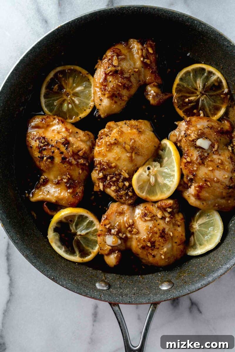 Honey garlic sauce poured on top of seared chicken thighs and lemon slices in a grey skillet