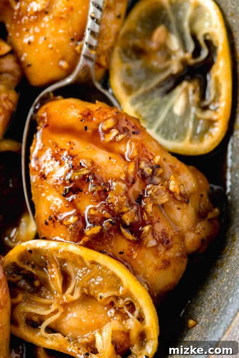 Honey garlic lemon pepper chicken thigh under a metal spoon with minced garlic on top of the chicken thigh