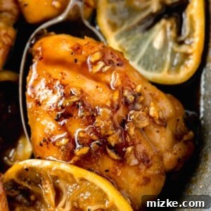 Honey garlic lemon pepper chicken thigh under a metal spoon with minced garlic on top of the chicken thigh