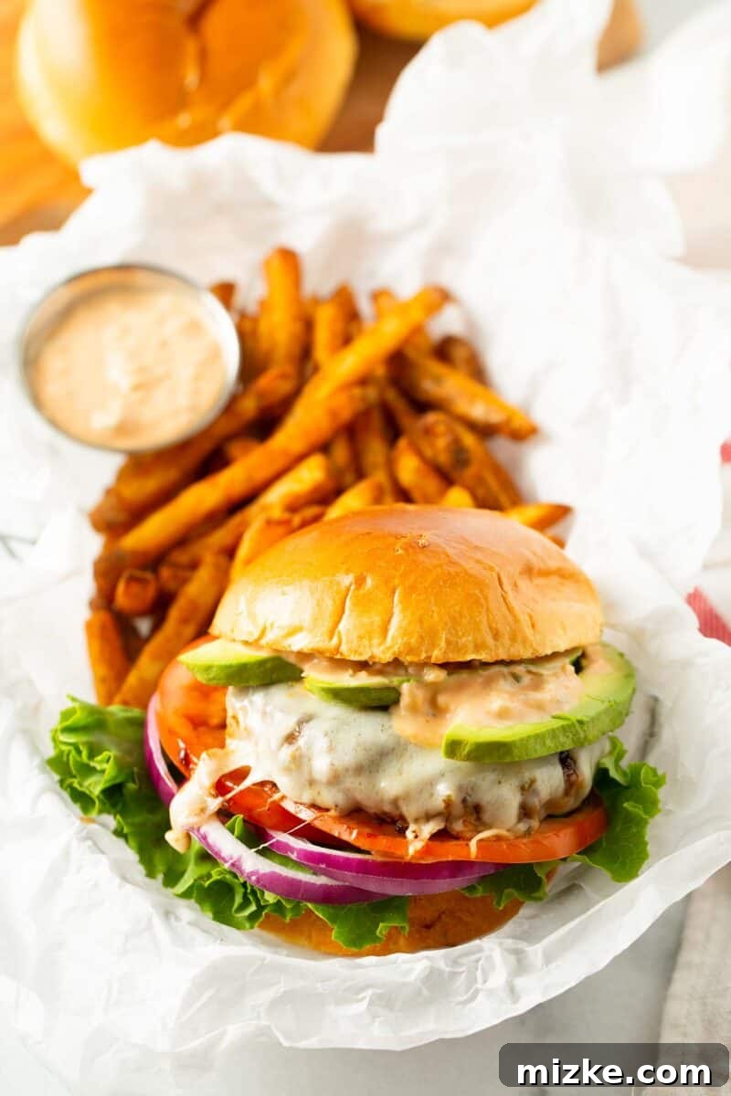 Golden State Delight 3 california burger in a basket lined with white parchment paper along with french fries and a condiment container