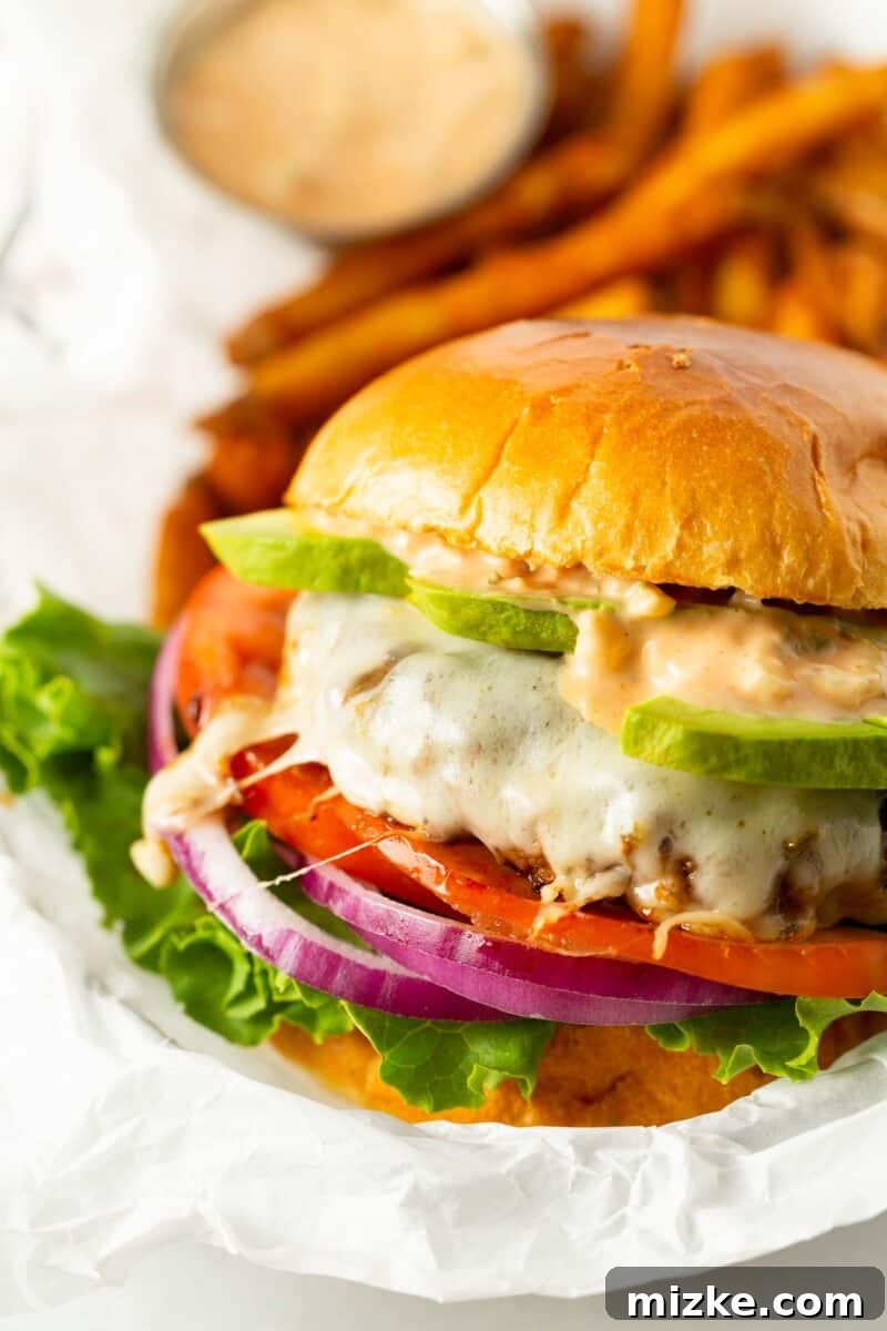 Golden State Delight 8 california burger between two brioche buns with burger sauce and avocado on a melted cheese burger patty with tomato, onion, and lettuce.