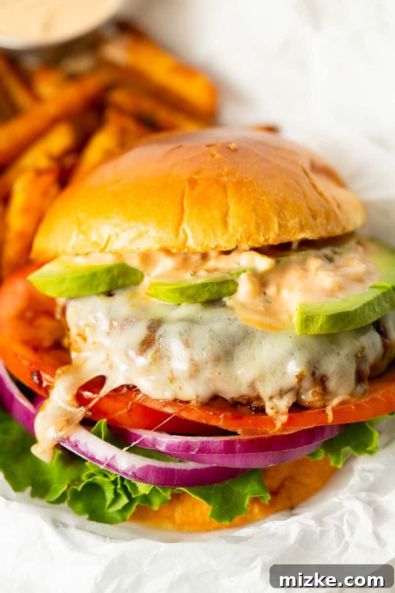 Golden State Delight 9 up close image of california burger with melted cheese on top of the burger patty sandwiched between brioche buns, loaded with fresh avocado slices, burger sauce, tomato, onion, and lettuce.