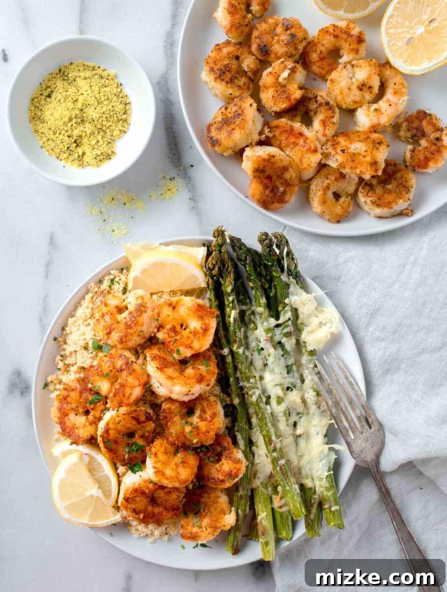 Zesty Lemon Pepper Shrimp 2 lemon pepper shrimp on a white plate on top of couscous with parmesan asparagus and lemon slices