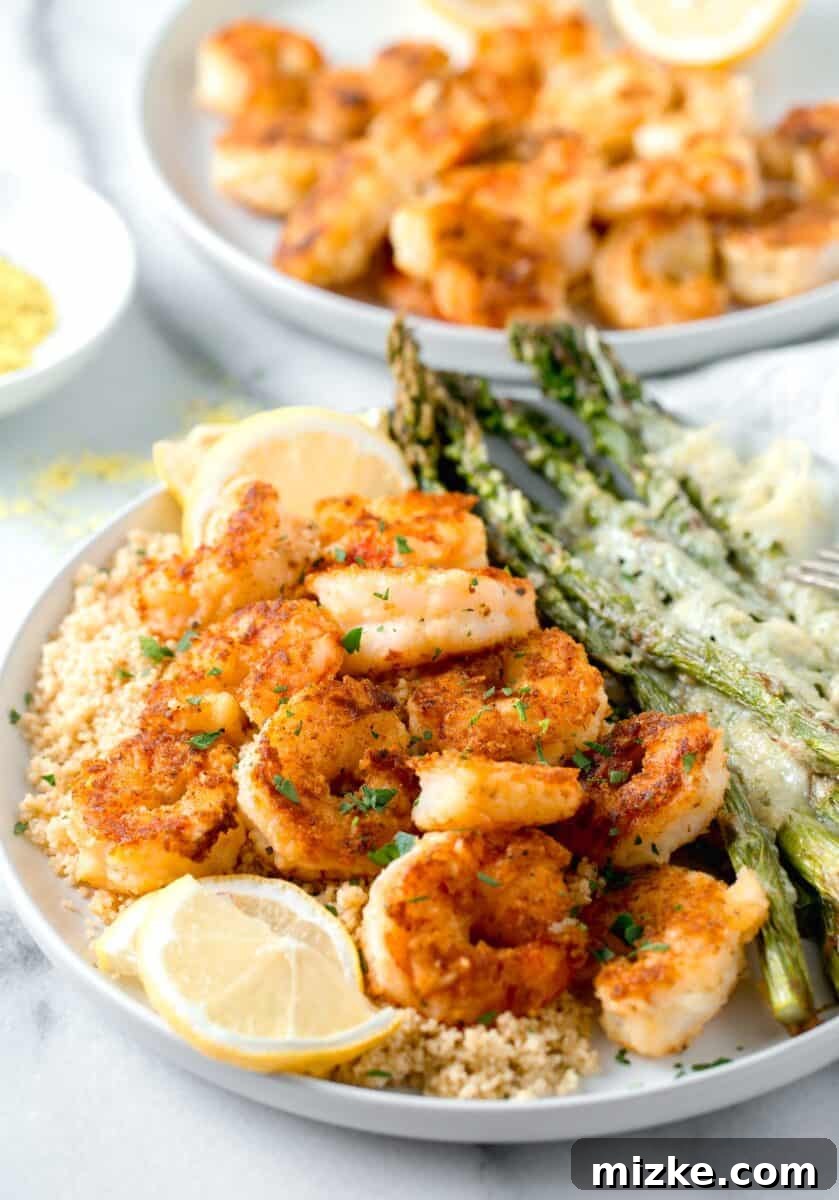 Zesty Lemon Pepper Shrimp 8 lemon pepper shrimp on top of couscous and next to parmesan crusted asparagus on a white plate with fresh lemon slices