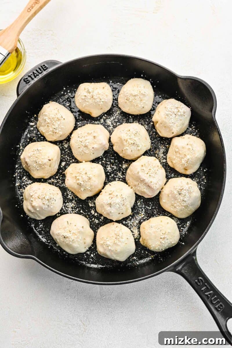 Seasoning the olive oil brushed pizza balls with parmesan, oregano, and garlic powder. The skillet of pizza balls, now brushed with olive oil and generously sprinkled with a mix of oregano, garlic powder, and grated Parmesan cheese, ready for the oven.