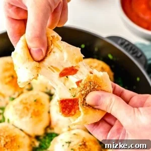 A hand pulling apart a freshly baked pizza ball, revealing its incredibly gooey, melted mozzarella cheese and savory pepperoni interior.