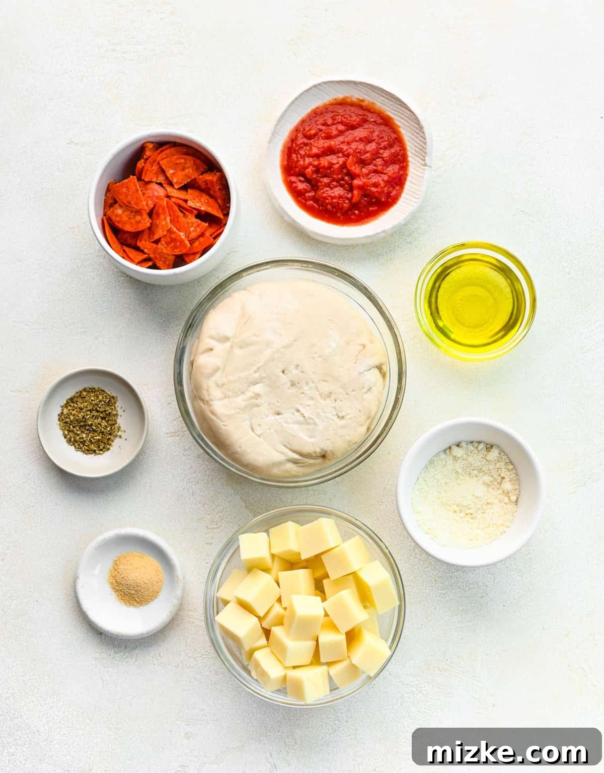Ingredients laid out for making easy pizza bites: pizza dough, mozzarella, pepperoni, olive oil, and parmesan. Various ingredients for Stuffed Pepperoni Pizza Balls neatly organized in separate bowls, including pizza dough, mozzarella cheese, pepperoni, olive oil, and seasonings.