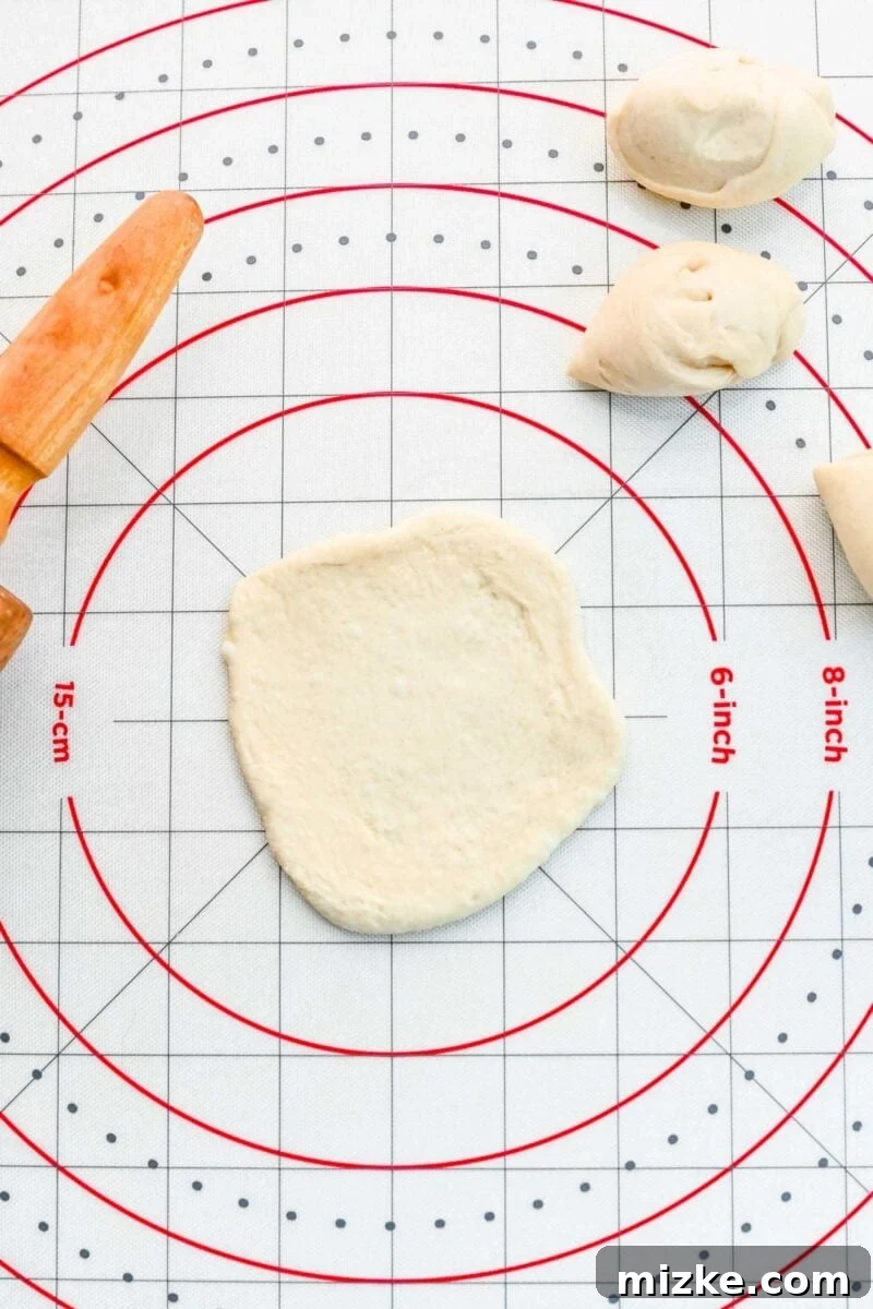 Rolling out individual pizza dough portions into small circles, preparing them for filling. A small portion of pizza dough being rolled out into a neat, thin circle, approximately ¼-inch thick, on a cutting board.