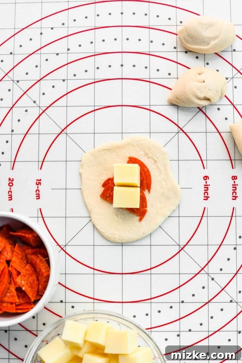 Placing mozzarella and pepperoni at the center of a rolled-out pizza dough circle. A small circle of pizza dough with mozzarella cheese cubes and quartered pepperoni slices placed neatly in its center, ready to be enclosed.