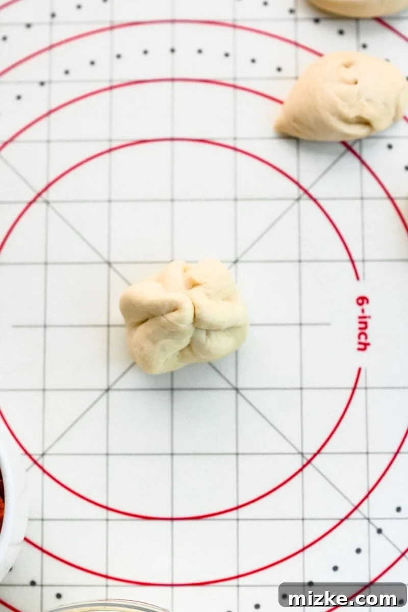 Carefully closing the pizza dough around the filling, ensuring a tight seal. Hands carefully pinching the edges of the pizza dough together around the mozzarella and pepperoni filling to form a sealed ball.