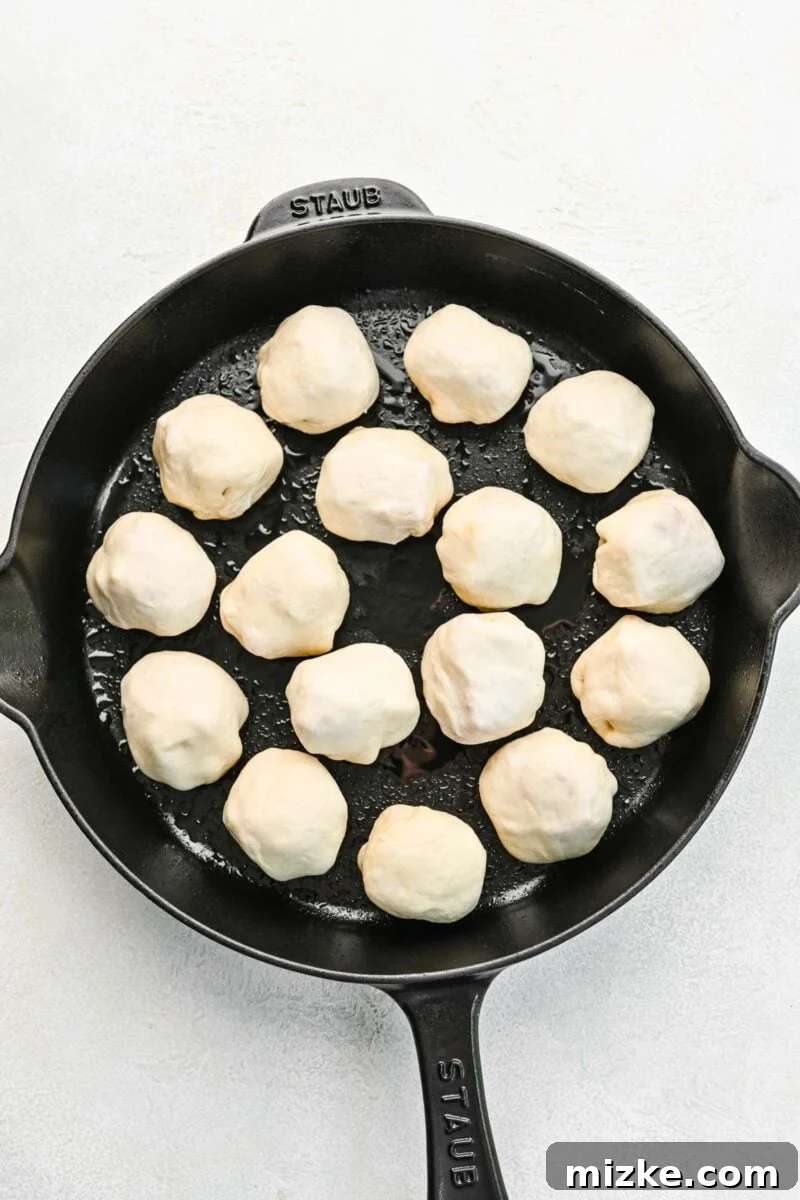 Arranging the prepared pizza balls, seam-side down, in a skillet. Several raw pizza balls, neatly arranged seam-side down in a greased cast iron skillet, ready for seasoning.