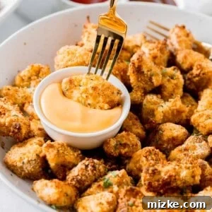 Air fried chicken nugget being dipped with a fork in a dipping sauce on a plate of other chicken nuggets