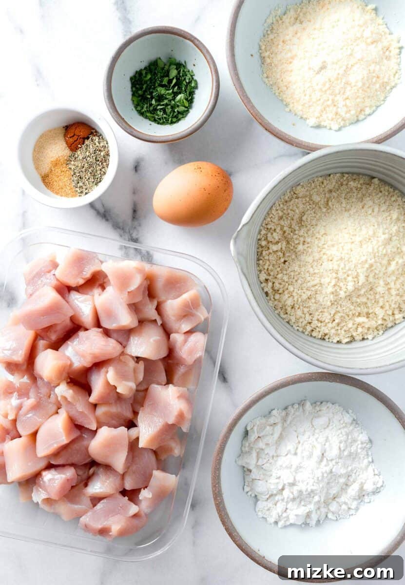 Ingredients laid out for making air fryer chicken nuggets, including chicken, egg, breadcrumbs, flour, and various spices