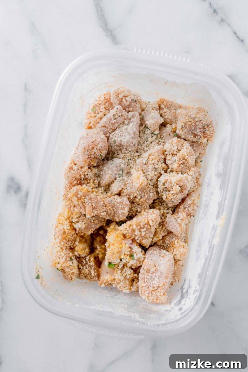 Chicken pieces thoroughly covered in the seasoned breadcrumb mixture within a plastic container