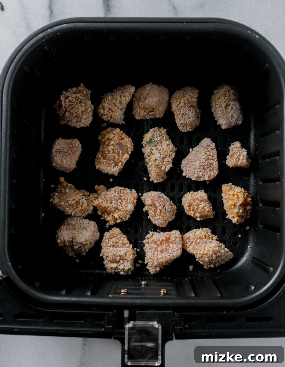 Uncooked, breaded chicken nuggets arranged in a single, even layer inside an air fryer basket